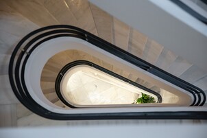 Vista interna de uma escadaria em espiral, com piso de mármore e uma planta na base.