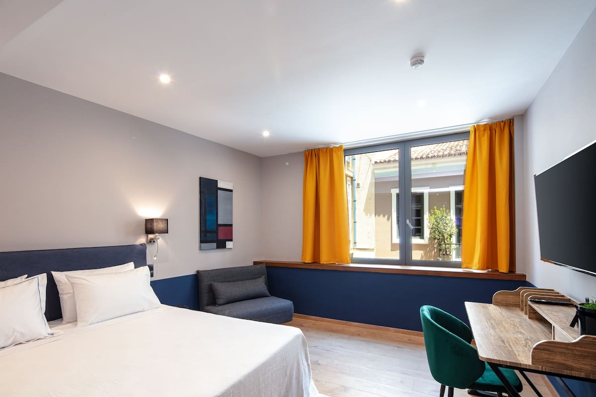 Une chambre d’hôtel avec un lit, un bureau, une chaise, une télévision et une fenêtre avec des rideaux.