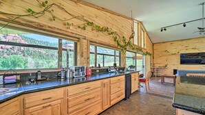 Eine moderne Küche mit Holzschränken, einer Granitarbeitsplatte und großen Fenstern mit Blick auf eine bewaldete Landschaft.