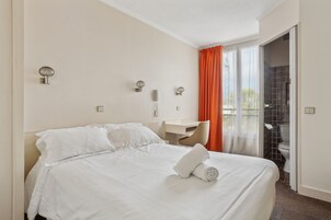 Habitación de hotel con cama, escritorio, teléfono y vistas al exterior a través de una ventana con cortinas naranjas.