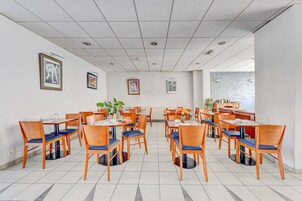 Un comedor amplio con varias mesas y sillas, obras de arte en las paredes y vistas al exterior a través de un ventanal.