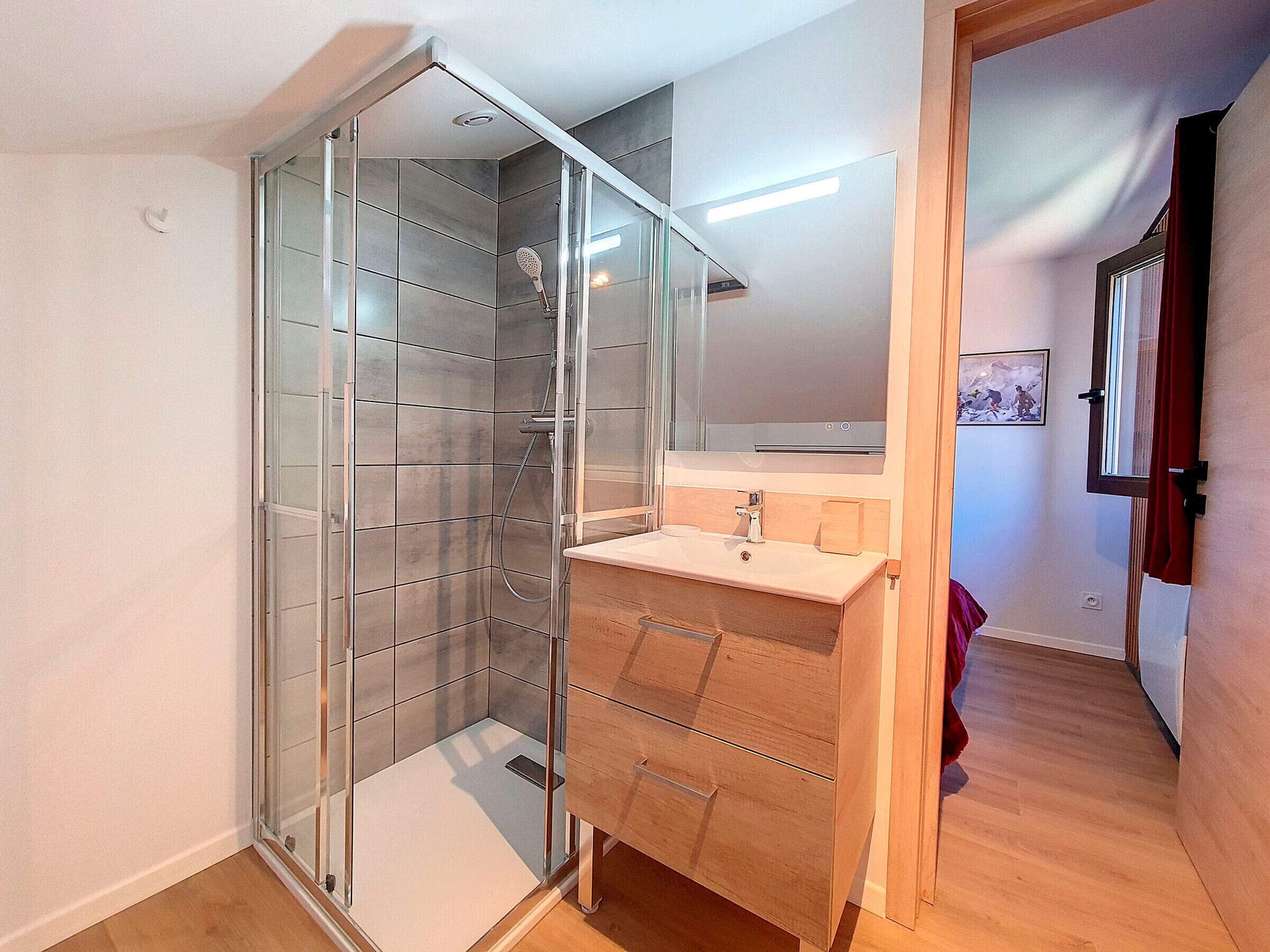 Un baño moderno con cabina de ducha de vidrio, tocador de madera y espejo sobre el lavabo.