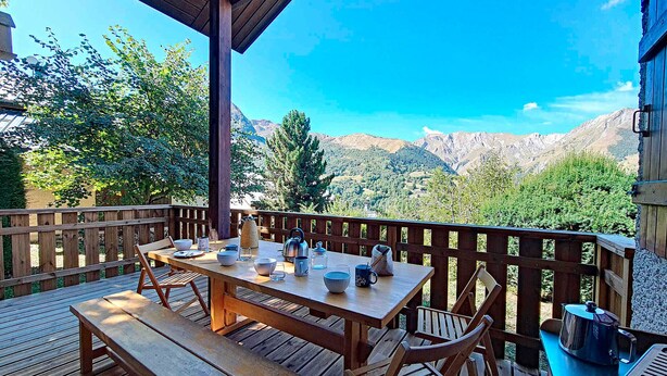 Une terrasse en bois avec une table et des chaises, offrant une vue sur un paysage montagneux.