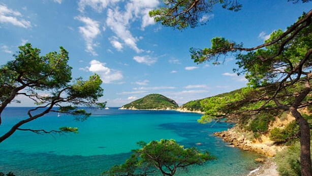 Un paysage côtier caractérisé par une eau turquoise cristalline, une plage de sable et des collines verdoyantes.