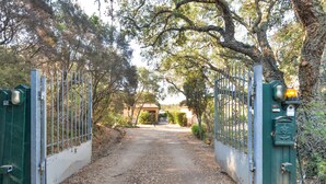 Une entrée fermée par un portail, avec un chemin de terre menant à un bâtiment doté d’un toit en tuiles.