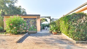 Un chemin pavé mène à un bâtiment doté d’une porte, entouré de verdure et surmonté d’un parasol blanc.