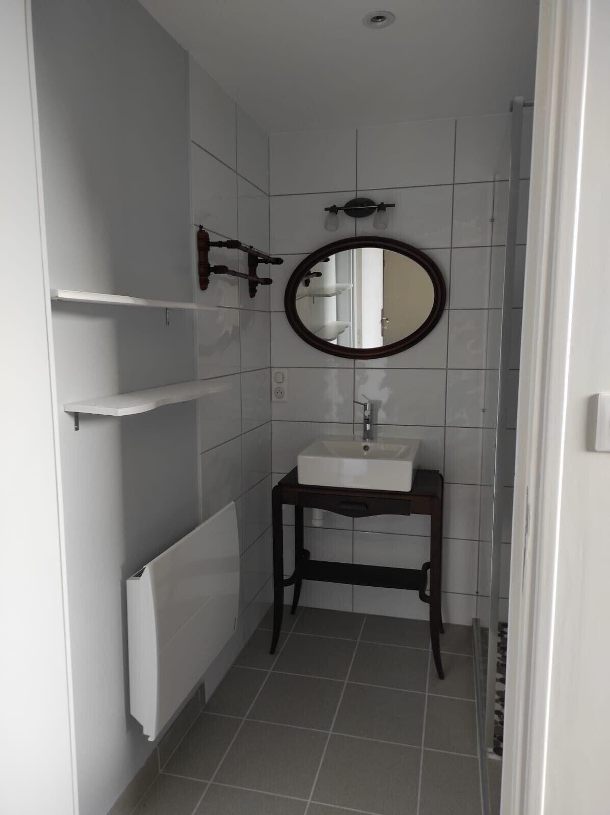 Ein Badezimmer mit einem weißen Waschbecken, einem runden Spiegel und einem Handtuchhalter.