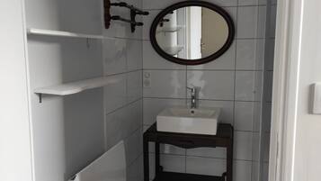 Ein Badezimmer mit einem weißen Waschbecken, einem runden Spiegel und einem Handtuchhalter.