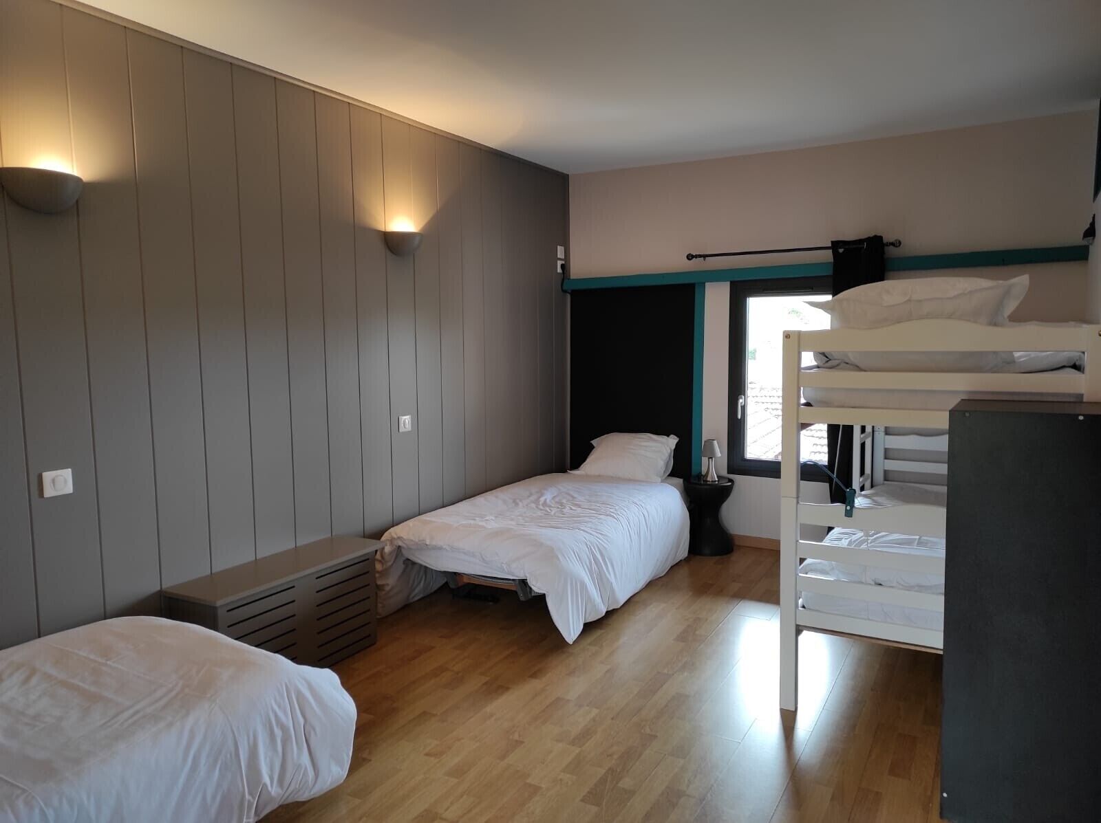 A bedroom with two single beds, a bunk bed, a window, and a wall-mounted light fixture.
