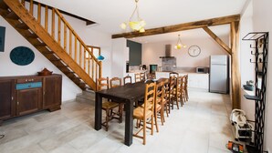 Un comedor con una mesa y sillas de madera, una escalera y una cocina al fondo.