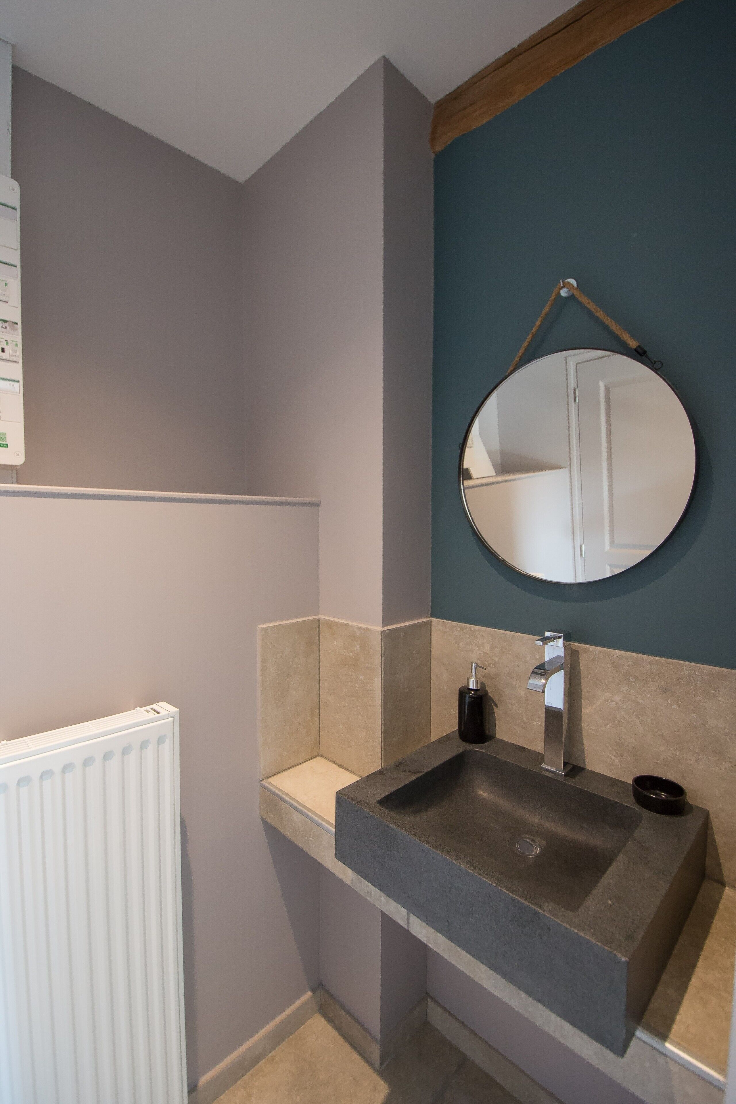 A bathroom with a rectangular sink, a round mirror, and a white radiator.