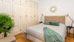Ein Schlafzimmer mit einem großen Bett, einem Kleiderschrank, einem runden Spiegel und einem kleinen Tisch mit einer Lampe.