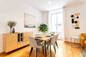 Un coin repas avec une table en bois dressée pour quatre personnes, entourée de chaises grises. Un buffet en bois, orné d’un vase et d’une plante, se trouve à gauche.