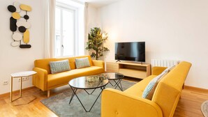 Ein modernes Wohnzimmer mit einer Couch, zwei Couchtischen, einem Fernseher und einer Pflanze.