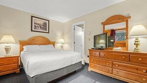 Una habitación de hotel con cama, televisión, cómoda y un cuadro en la pared.