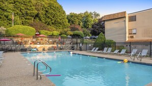 A swimming pool with lounge chairs, a fenced area with tables and umbrellas, and a building in the background. - Lakes Region Escape | Private Balcony Near Weirs Beach (Laconia)