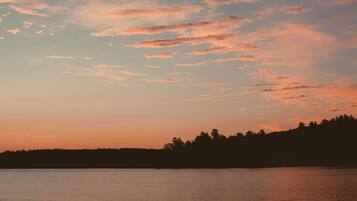 A sunset over a calm body of water with a silhouette of a forested hill in the distance.