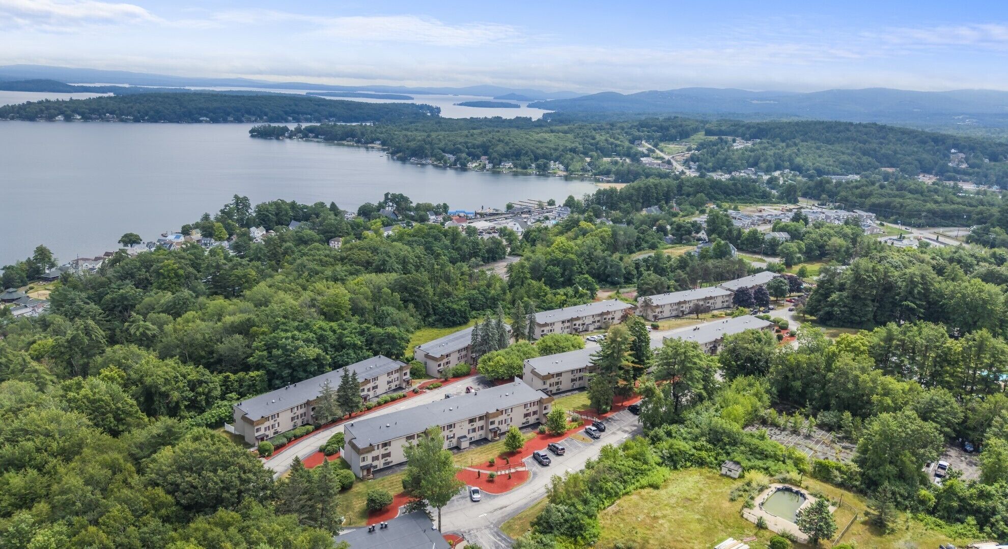 A residential area with multiple apartment buildings surrounded by dense greenery and a large body of water in the background.