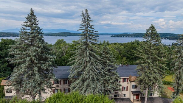 A residential area with multiple buildings, a lake, and mountains in the background. - Lakes Region Escape | Private Balcony Near Weirs Beach (Laconia)