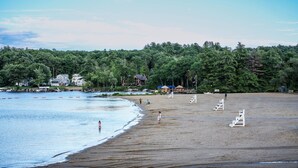 A beach with a sandy shore, a few people, and a forested area in the background. - Lakes Region Escape | Private Balcony Near Weirs Beach (Laconia)