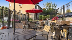 An outdoor patio with round tables and chairs, red umbrellas, and a barbecue grill. - Lakes Region Escape | Private Balcony Near Weirs Beach (Laconia)