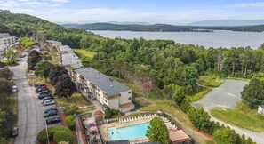 Um hotel com piscina, estacionamento e vista para um lago e montanhas.