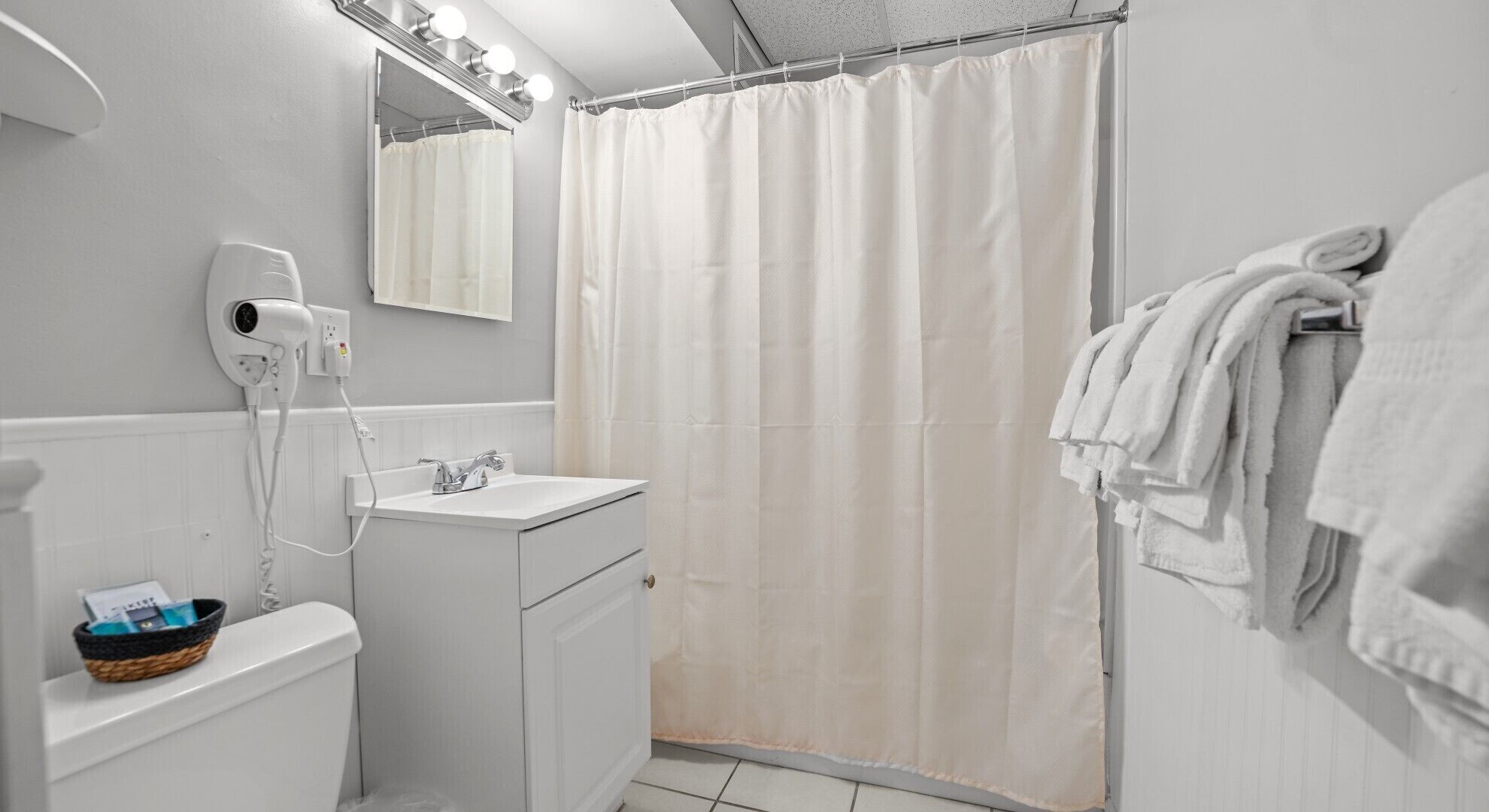 A bathroom with a white sink, a mirror with lights, a shower curtain, and a towel rack.