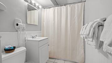 A bathroom with a white sink, a mirror with lights, a shower curtain, and a towel rack.