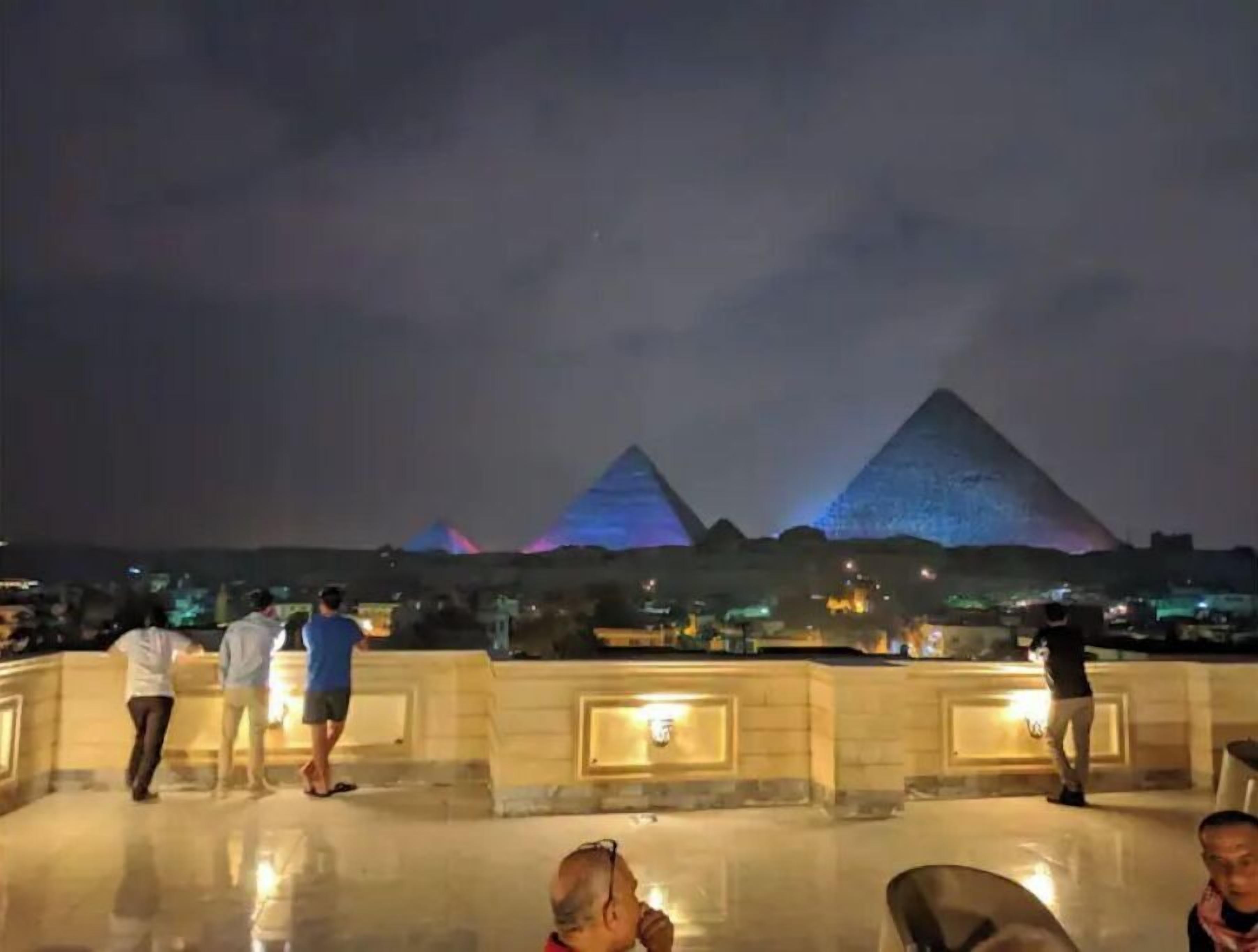 Une vue nocturne des pyramides, avec des personnes se promenant sur une terrasse.