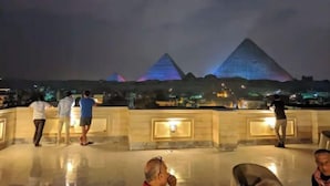 A nighttime view of the pyramids with people walking on a terrace. - pyramids kingdom apartment (الجيزة)