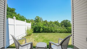 Blick von einer Veranda mit zwei Stühlen, die auf einen weißen Zaun und einen Rasen mit Bäumen zeigen.