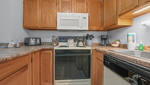 Una cocina con armarios de madera, microondas, tostadora, hervidor, cafetera y lavavajillas.
