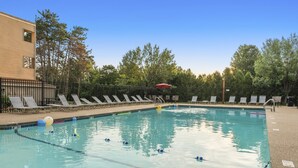 Una piscina con sillas de descanso y una cerca, rodeada de árboles.