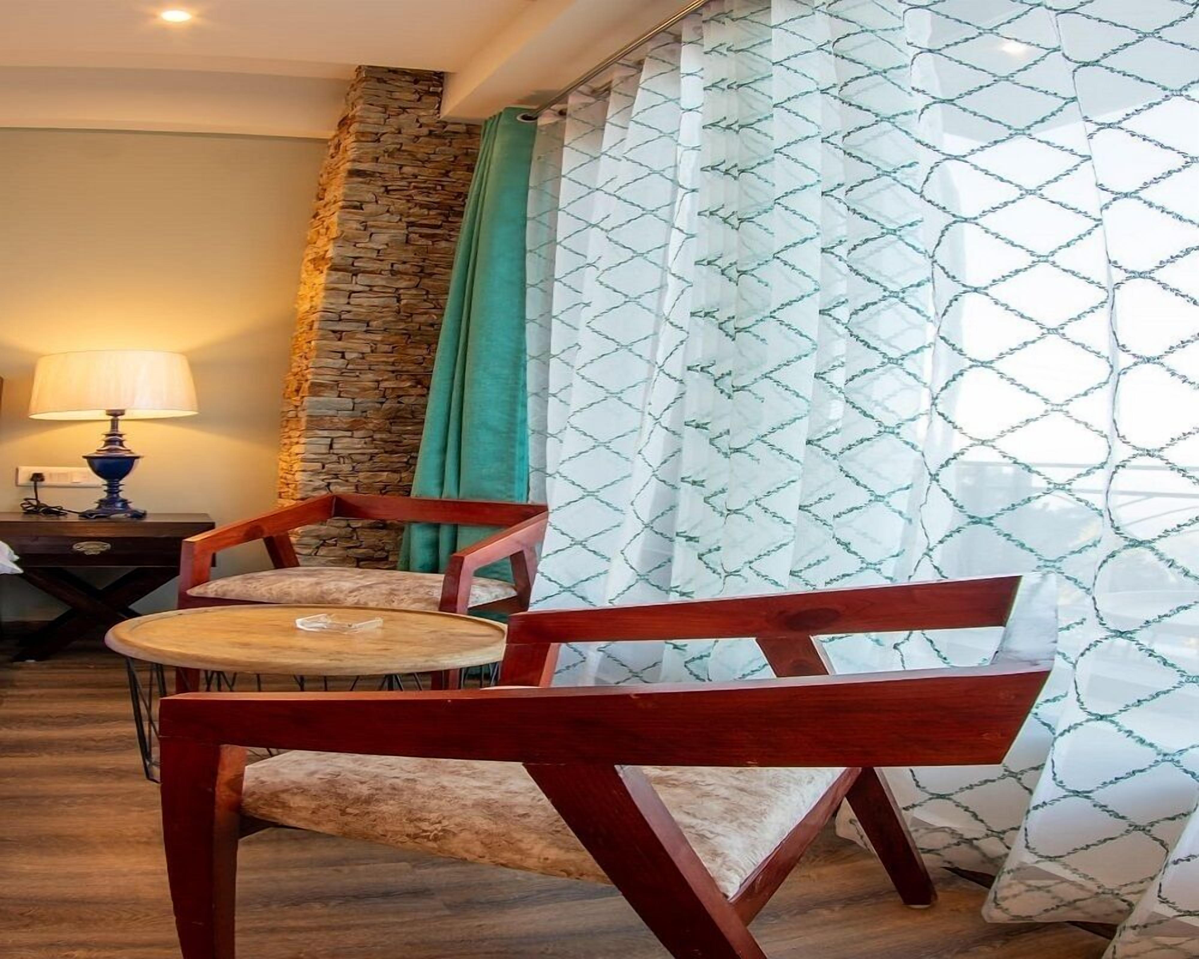 Una habitación con una pared de acento de piedra, una mesa redonda con dos sillas, una lámpara y cortinas estampadas.