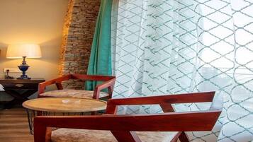 Una habitación con una pared de acento de piedra, una mesa redonda con dos sillas, una lámpara y cortinas estampadas.