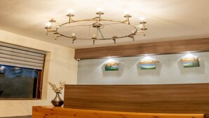 A reception area with a wooden reception desk, a modern chandelier, and three framed landscape paintings on the wall. - The Himalayan Voyage (Ranikhet)