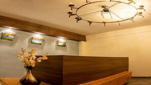 A reception desk with a wooden base, a vase with flowers, and a unique ceiling light fixture. - The Himalayan Voyage (Ranikhet)