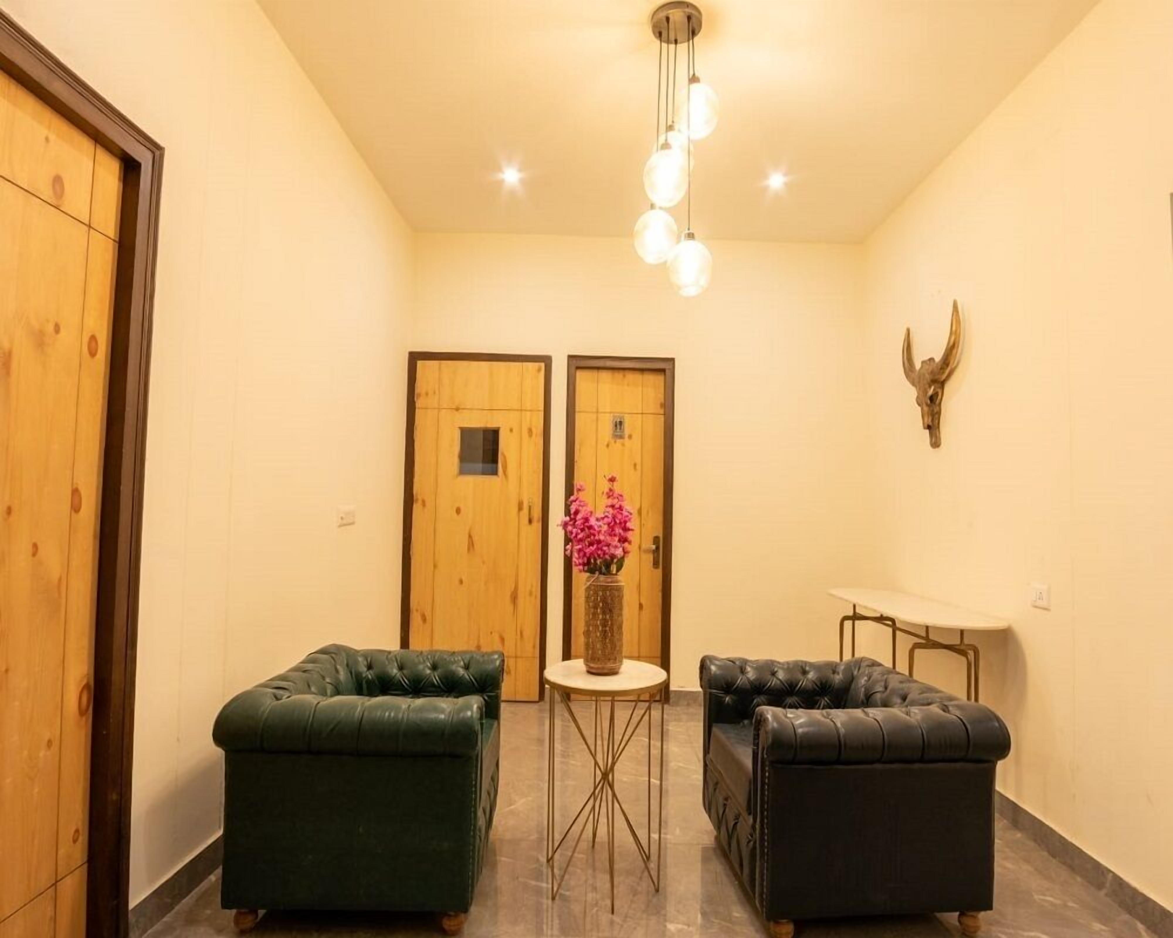 A hallway with two wooden doors, a small round table with a vase of pink flowers, and two green leather sofas.