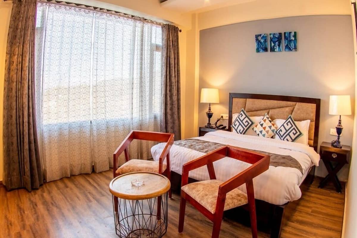 A hotel room with a bed, two chairs, a small round table, and a nightstand with lamps.