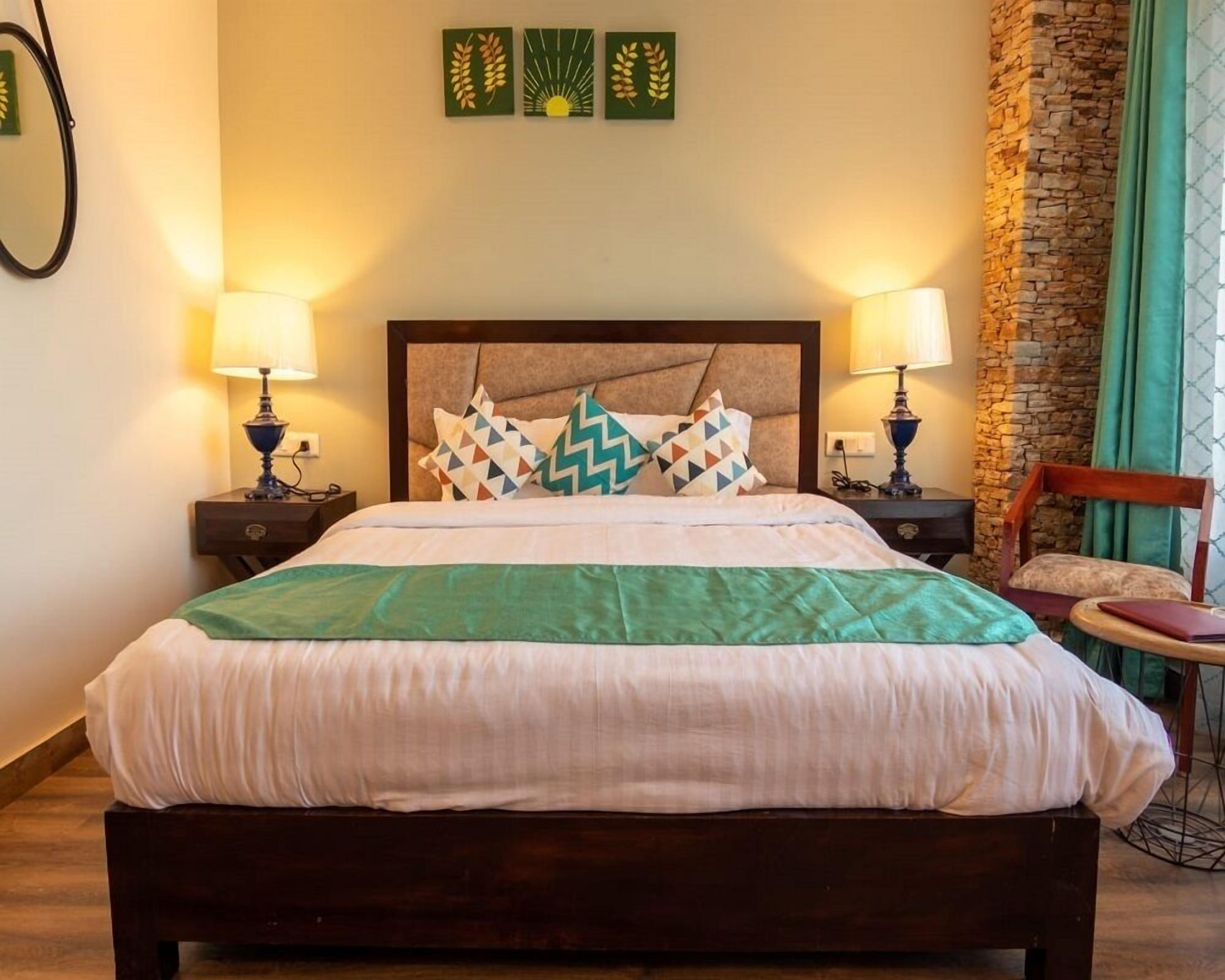 Una cama bien hecha con un edredón verde, dos lámparas de noche y una pared con tres cuadros enmarcados.