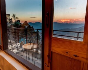 A balcony with metal chairs and a small table, overlooking a mountainous landscape during sunset. - The Himalayan Voyage (Ranikhet)
