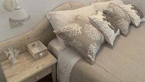 Una cama bien hecha con cabecera de madera, una mesita de noche con un objeto decorativo y una lámpara de pared.