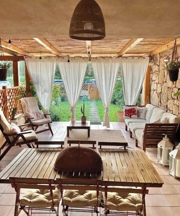 A covered patio area with wooden furniture, including a table and chairs, and a sofa.