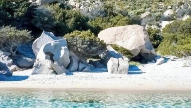 Una playa con agua azul cristalina y formaciones rocosas.