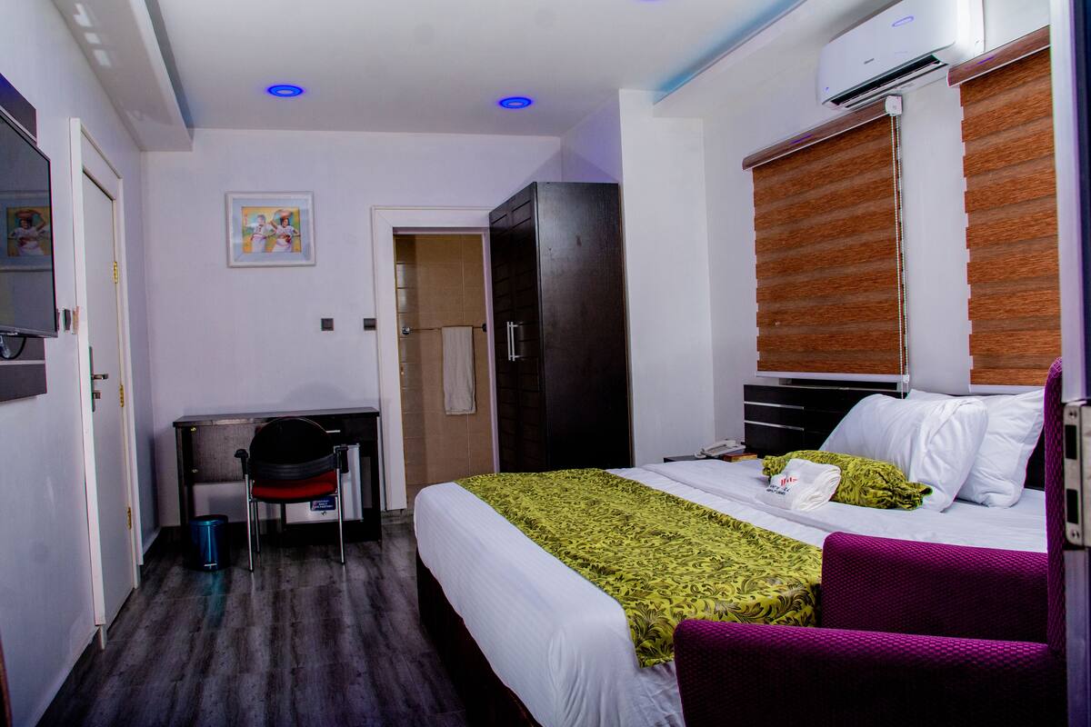 Quarto de hotel com cama, escrivaninha, cadeira e ar condicionado.