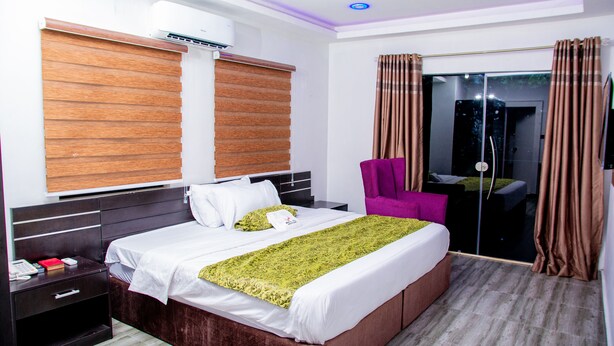 Una habitación de hotel con una cama grande, una mesita de noche, una silla y una puerta corrediza de vidrio que da a un balcón.