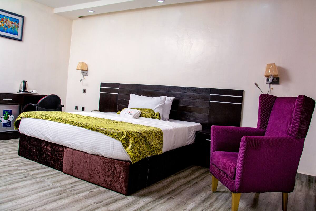 Quarto de hotel com cama, escrivaninha, cadeira e abajur.