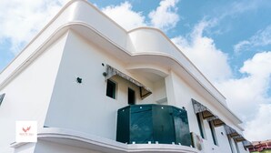 Un edificio moderno con fachada curva, un balcón con cerramiento de vidrio y un cielo azul despejado al fondo.