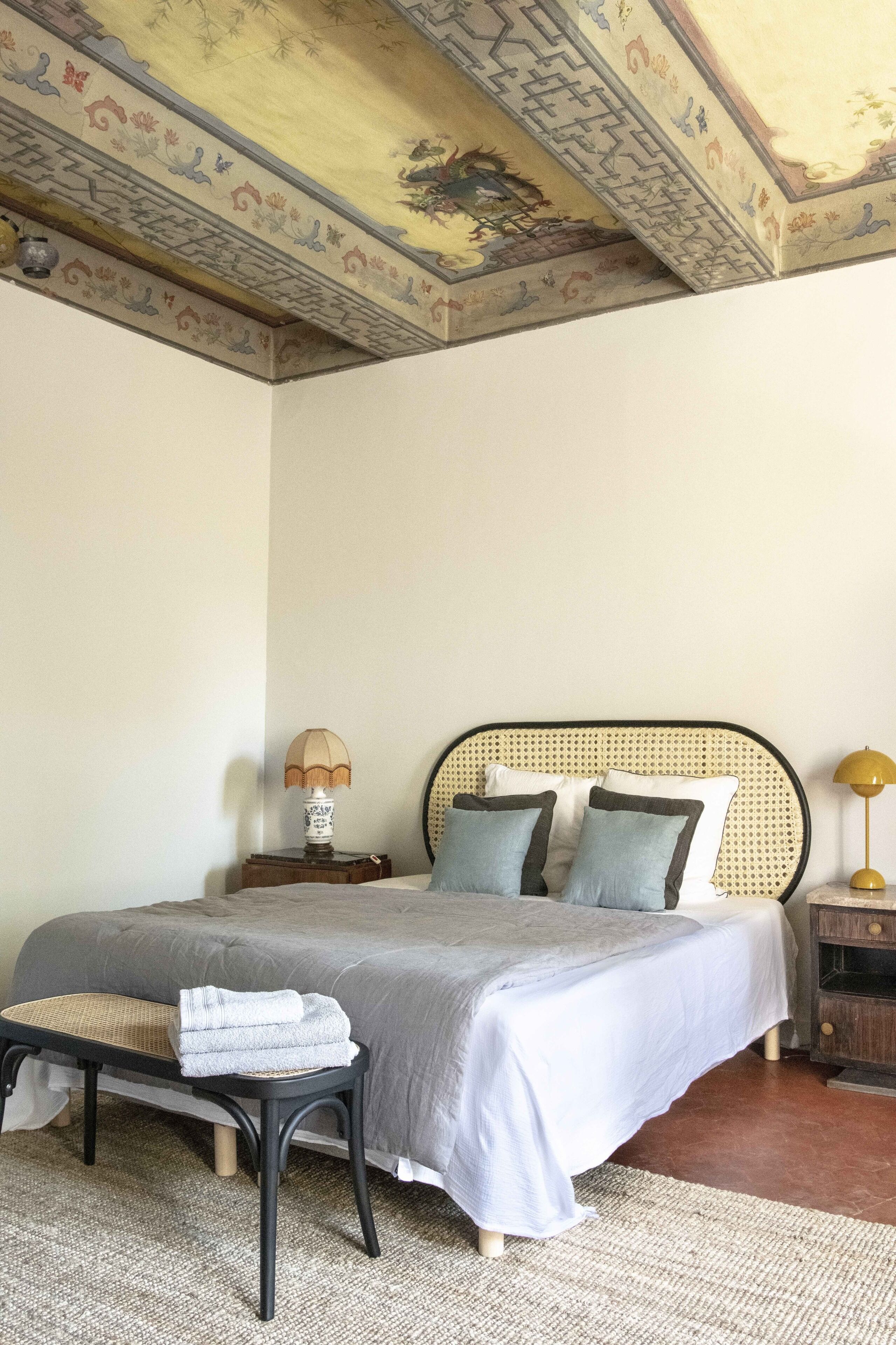 Un dormitorio con una cama, un banco, una mesita de noche y una lámpara.