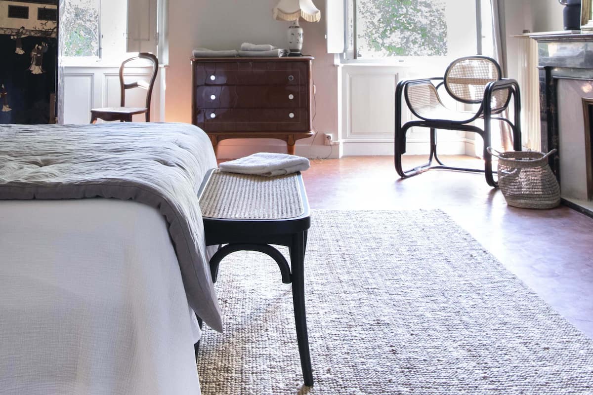 A bedroom with a large bed, a chair, a dresser, and a window with a view of trees.